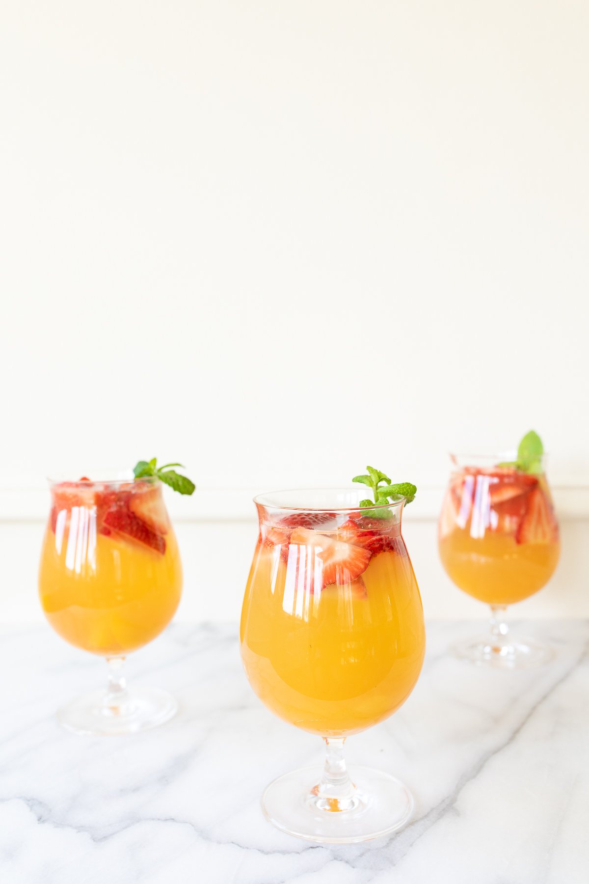 Three glasses of Moscato sangria garnished with strawberries, peaches and mint.