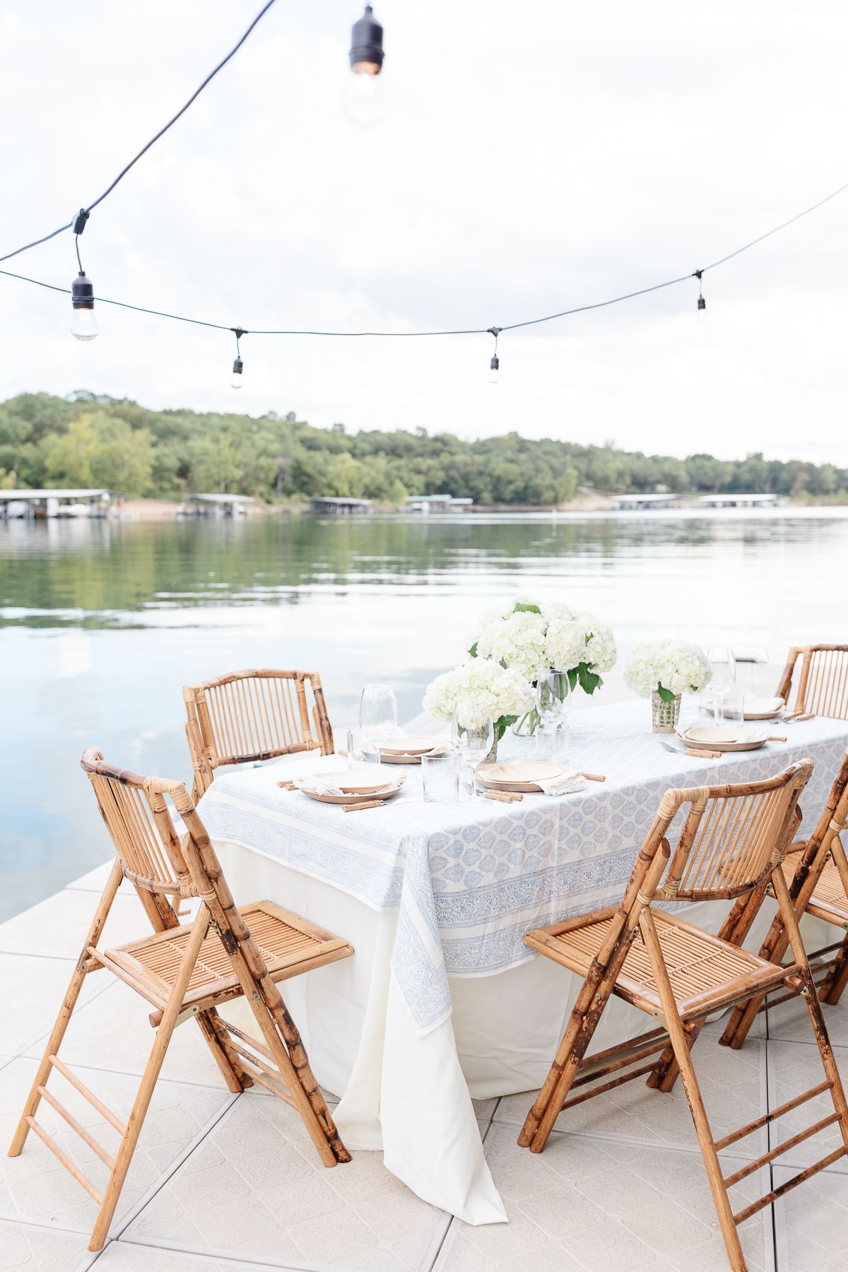 A mother's day brunch set up with white flowers and bamboo chairs on a dock at a lake