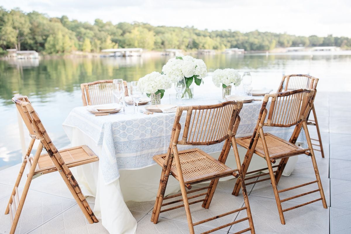 A mother's day brunch set up with white flowers and bamboo chairs on a dock at a lake