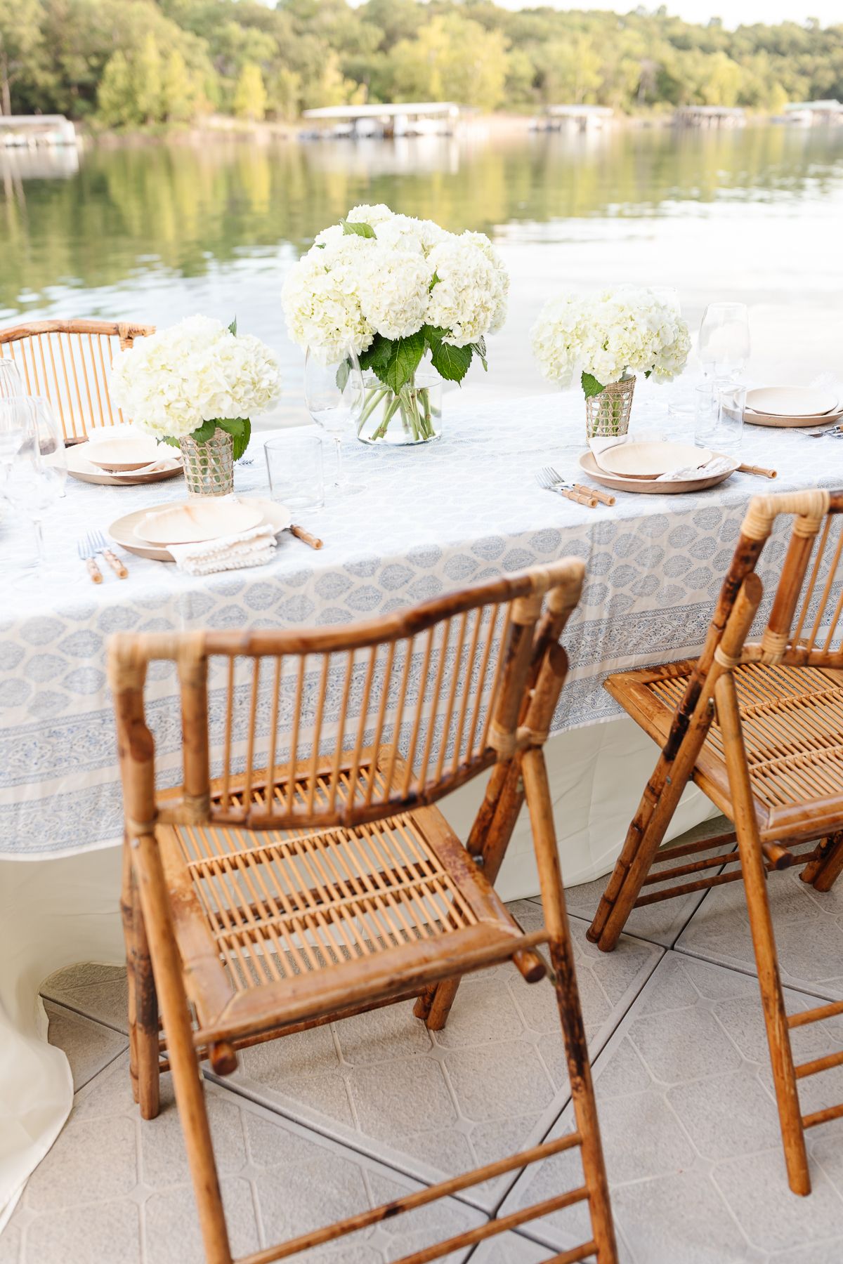 A mother's day brunch set up with white flowers and bamboo chairs on a dock at a lake