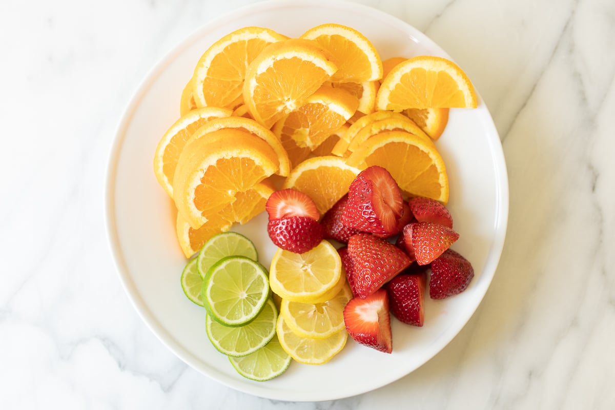 A white plate of sliced fruits for Spanish sangria.