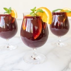 Traditional red sangria in stemware, garnished with fresh mint and orange slices.