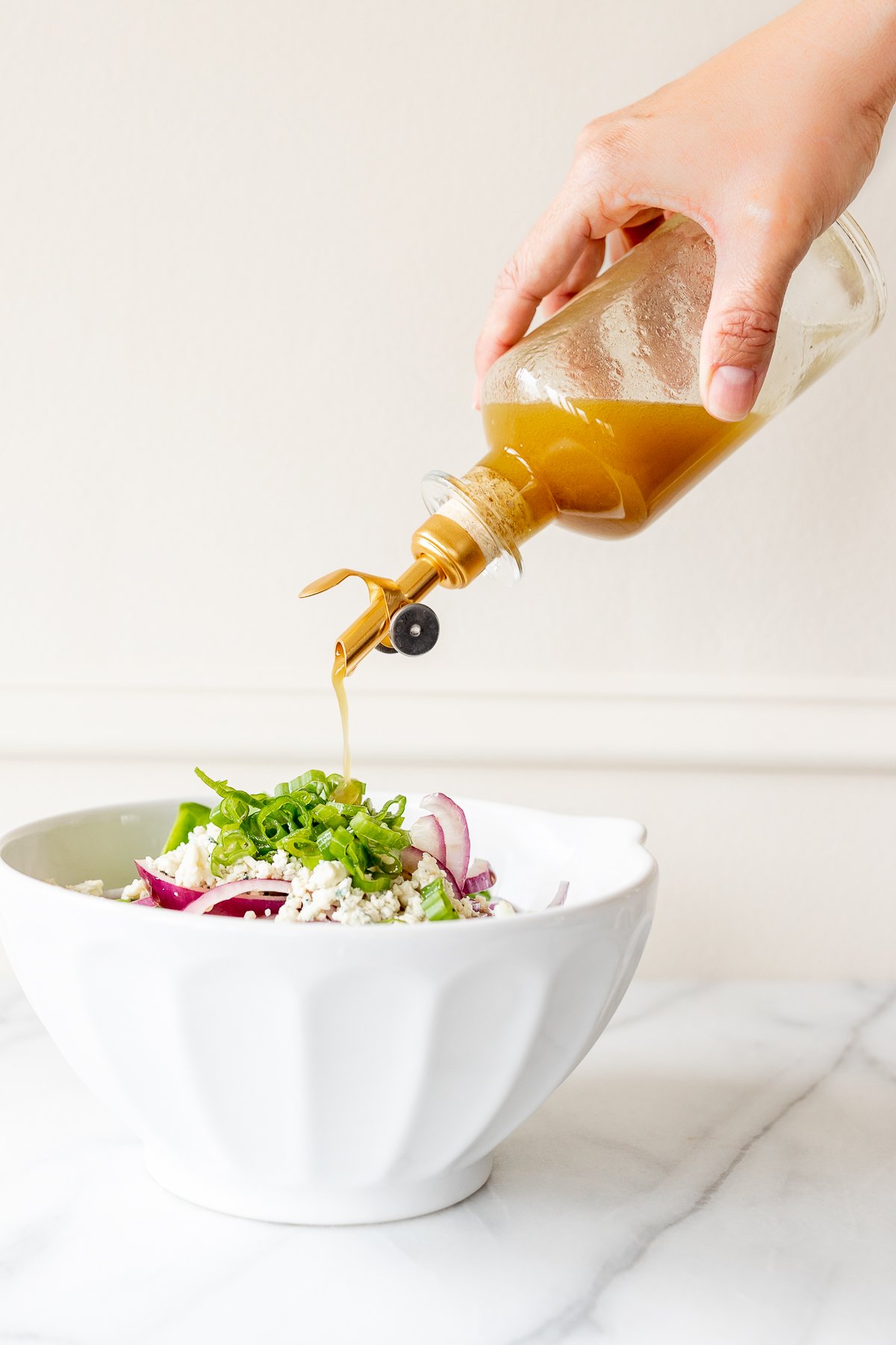 A bottle of dressing being poured over a salad in a white bowl.