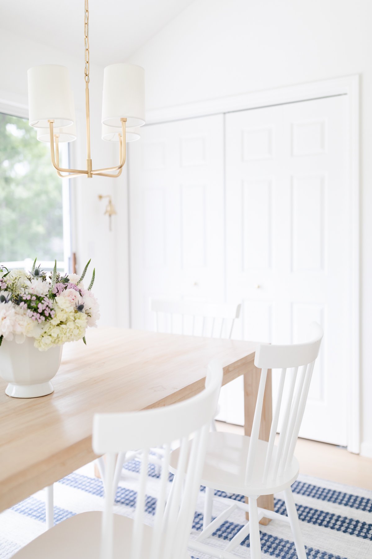 A teak dining table with white chairs and a white chandelier.