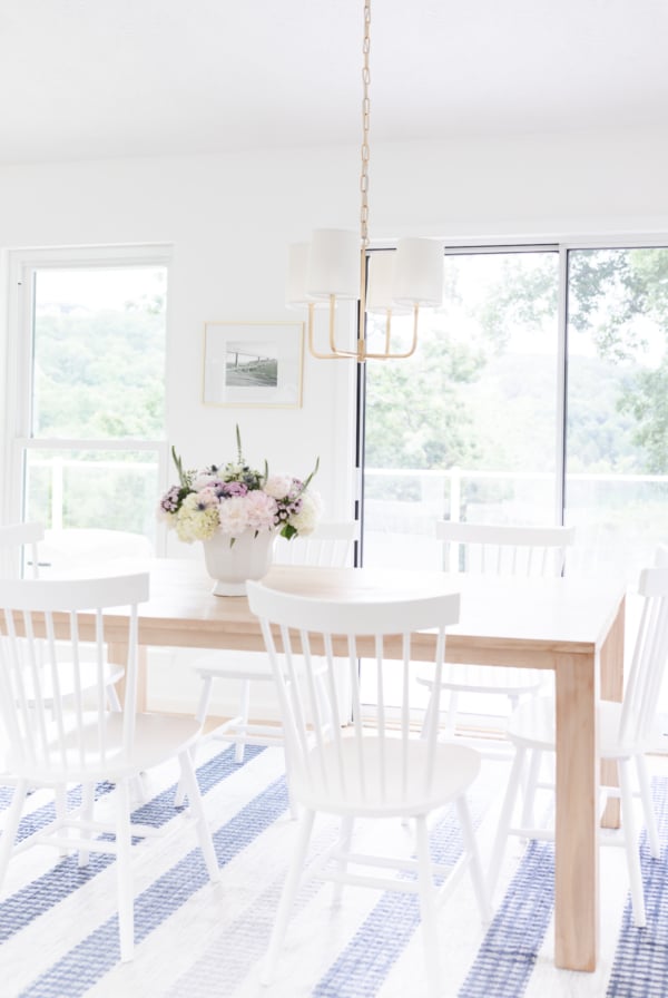 A teak dining table with white chairs and a vase of flowers.