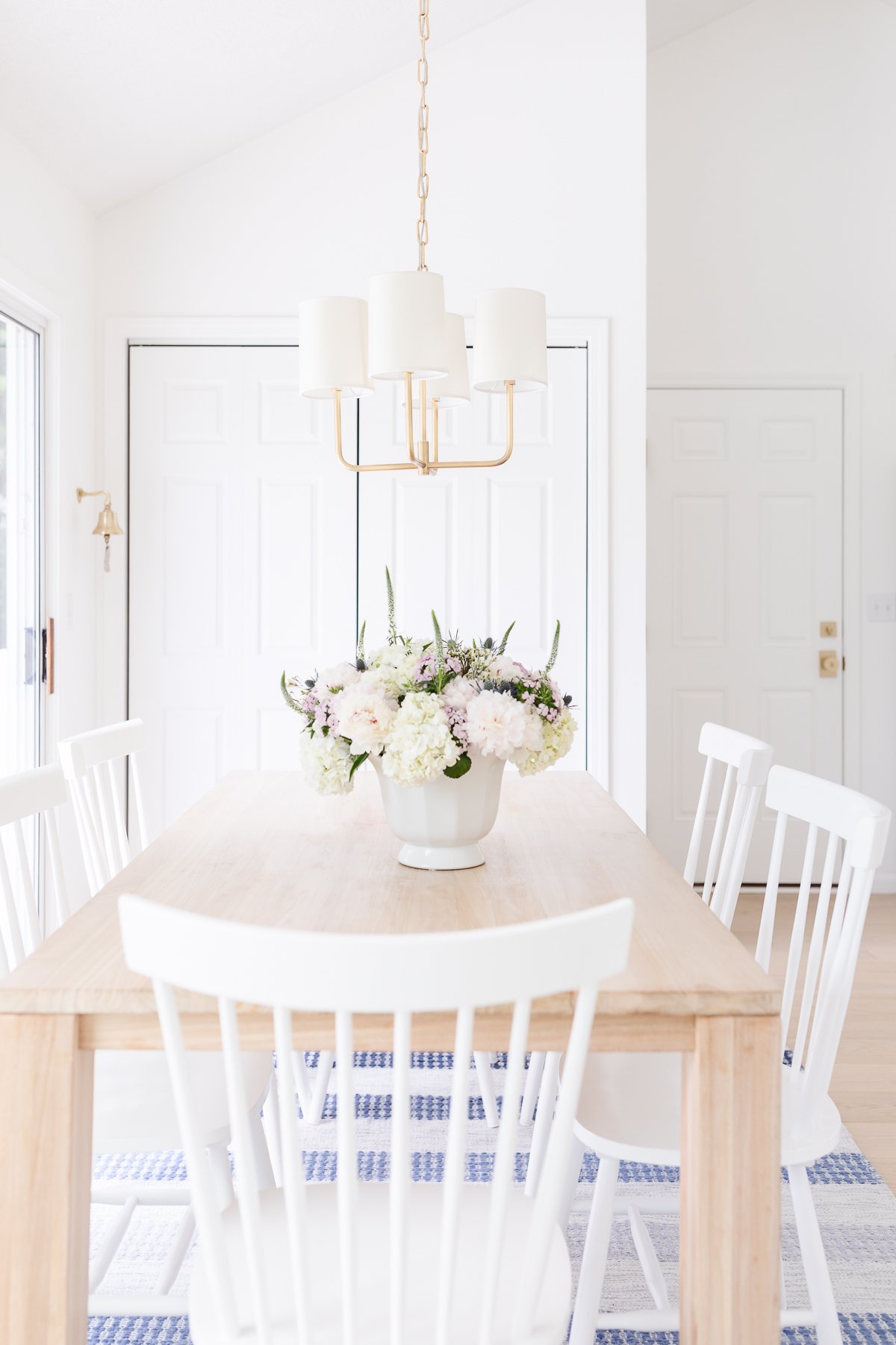 A teak dining table with white chairs and a vase of flowers.