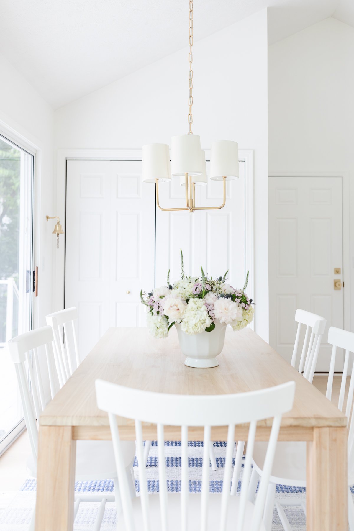 A teak table with white chairs and a vase of flowers.
