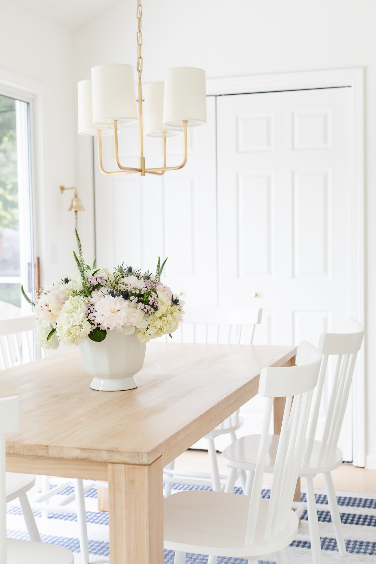 A white vase with flowers on a teak dining table.