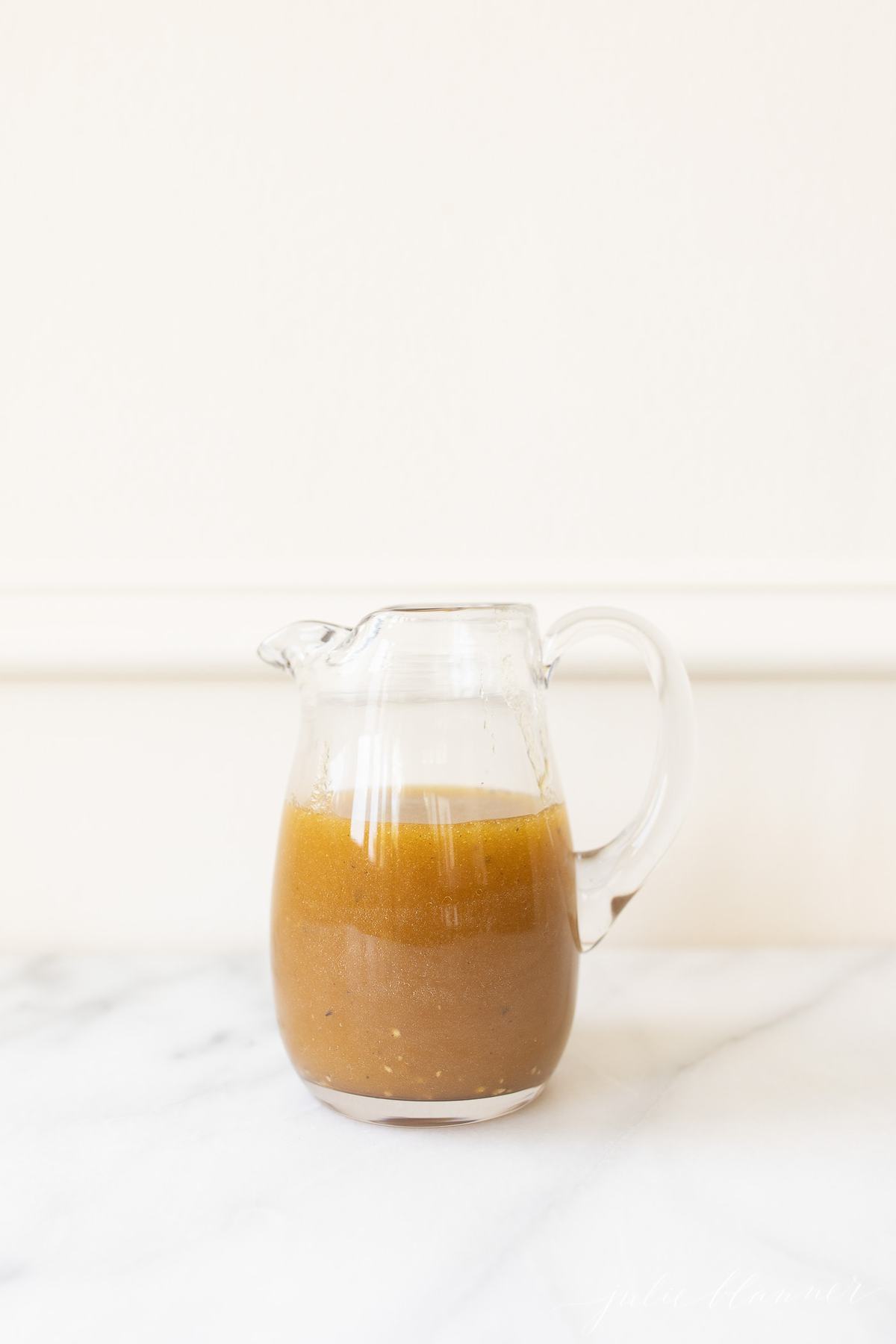 Balsamic dressing in a clear pitcher on a marble surface. 