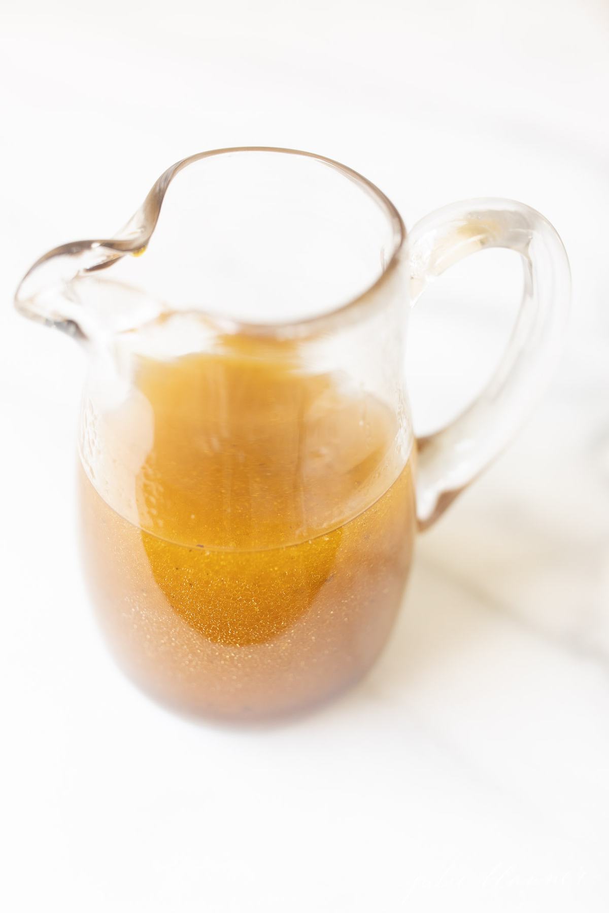 Balsamic vinaigrette in a clear pitcher on a marble surface. 