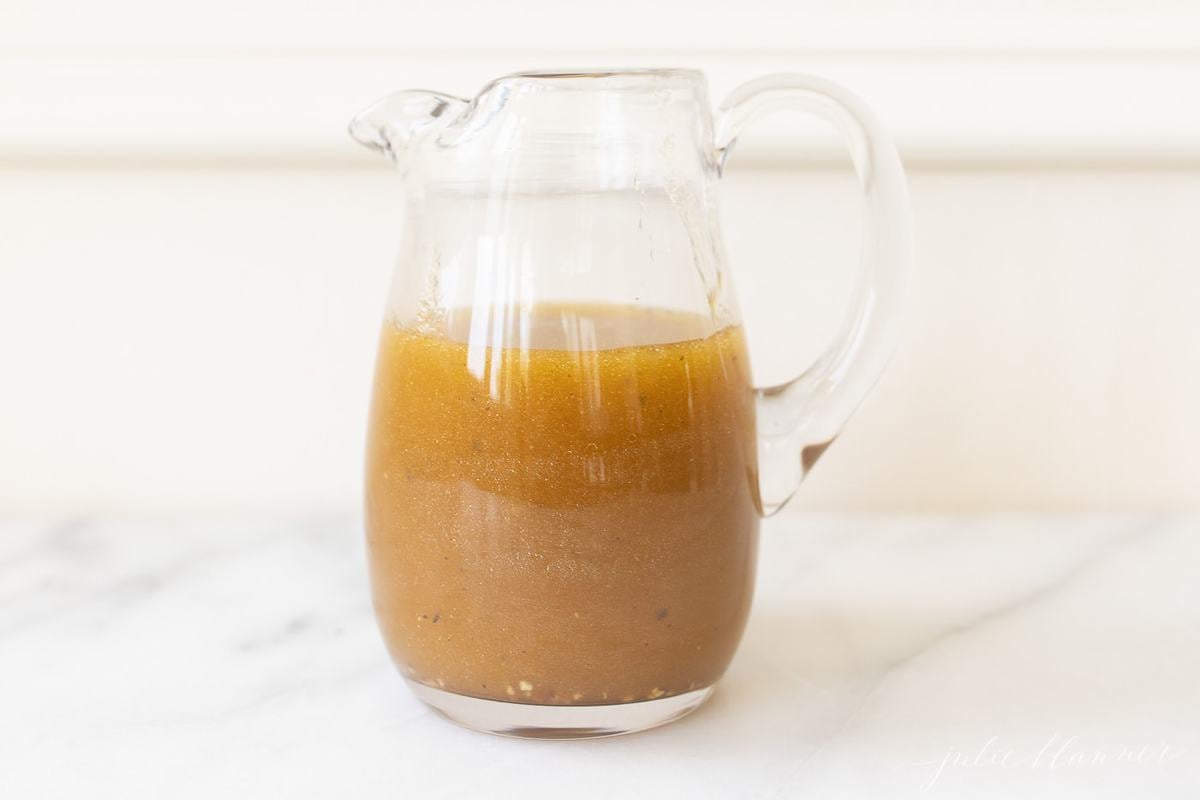 Balsamic vinegar dressing in a clear pitcher on a marble surface. 