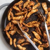 chicken covered in cajun seasoning in cast iron with tongs