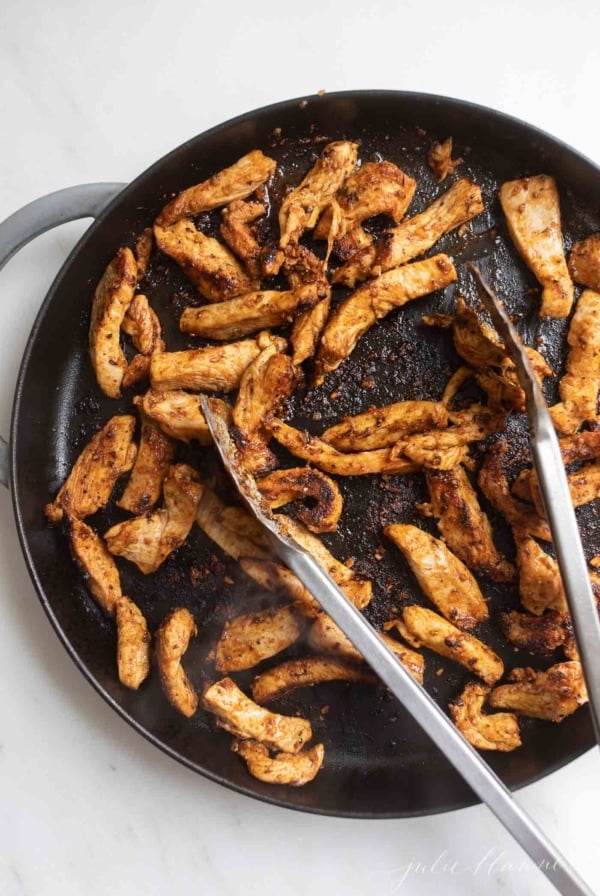 chicken covered in cajun seasoning in cast iron with tongs