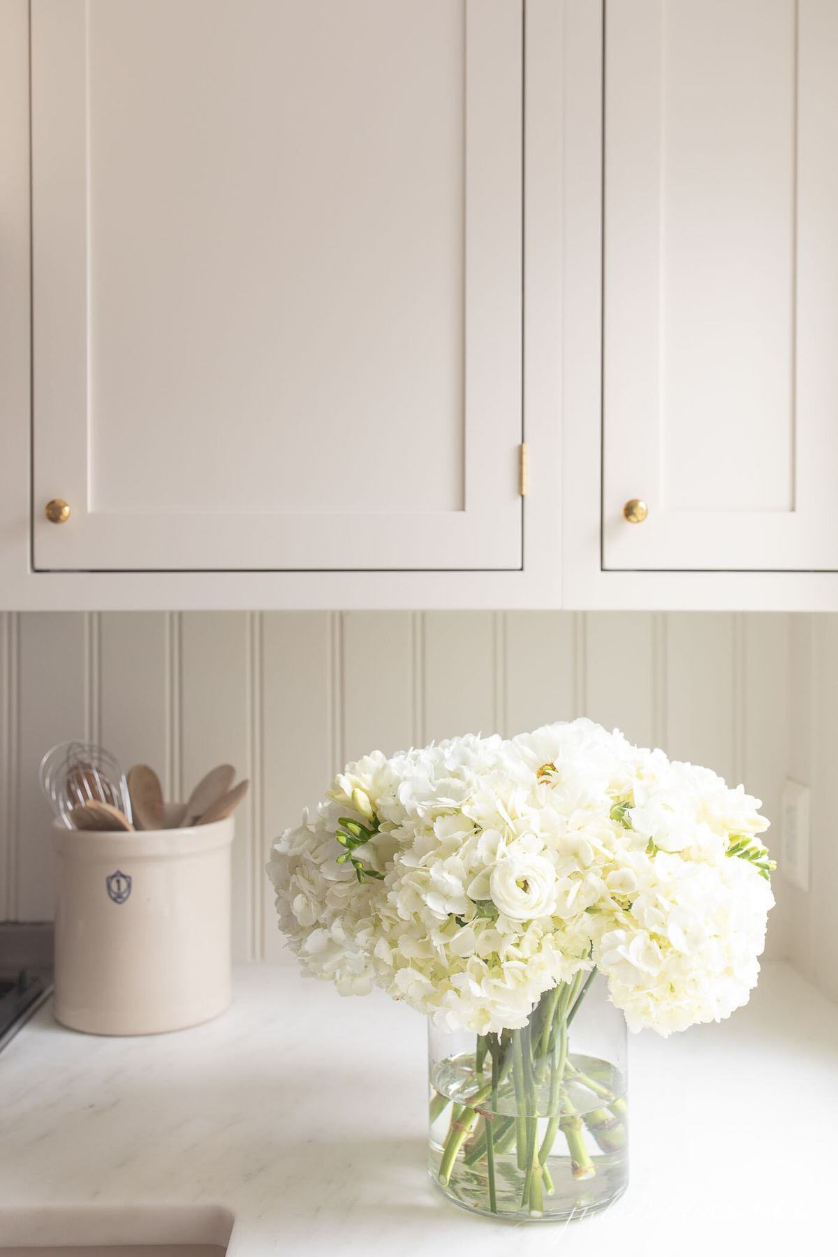 Flowers in a glass vase on a white kitchen countertop. 