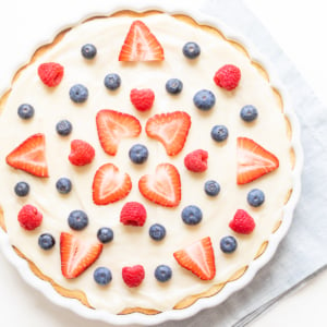 A freshly prepared fruit pizza with creamy filling, garnished with strawberries, blueberries, and raspberries.