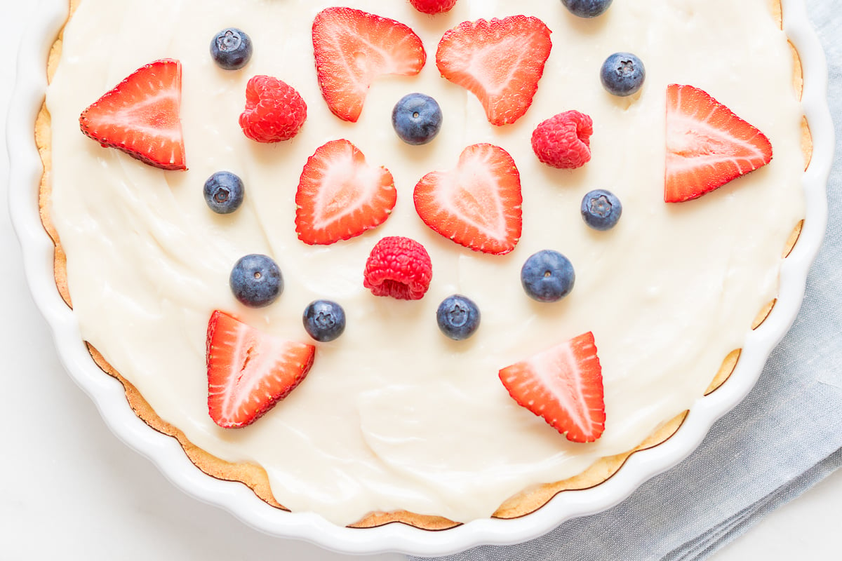 A freshly prepared fruit pizza topped with cream and garnished with strawberries, blueberries, and raspberries.