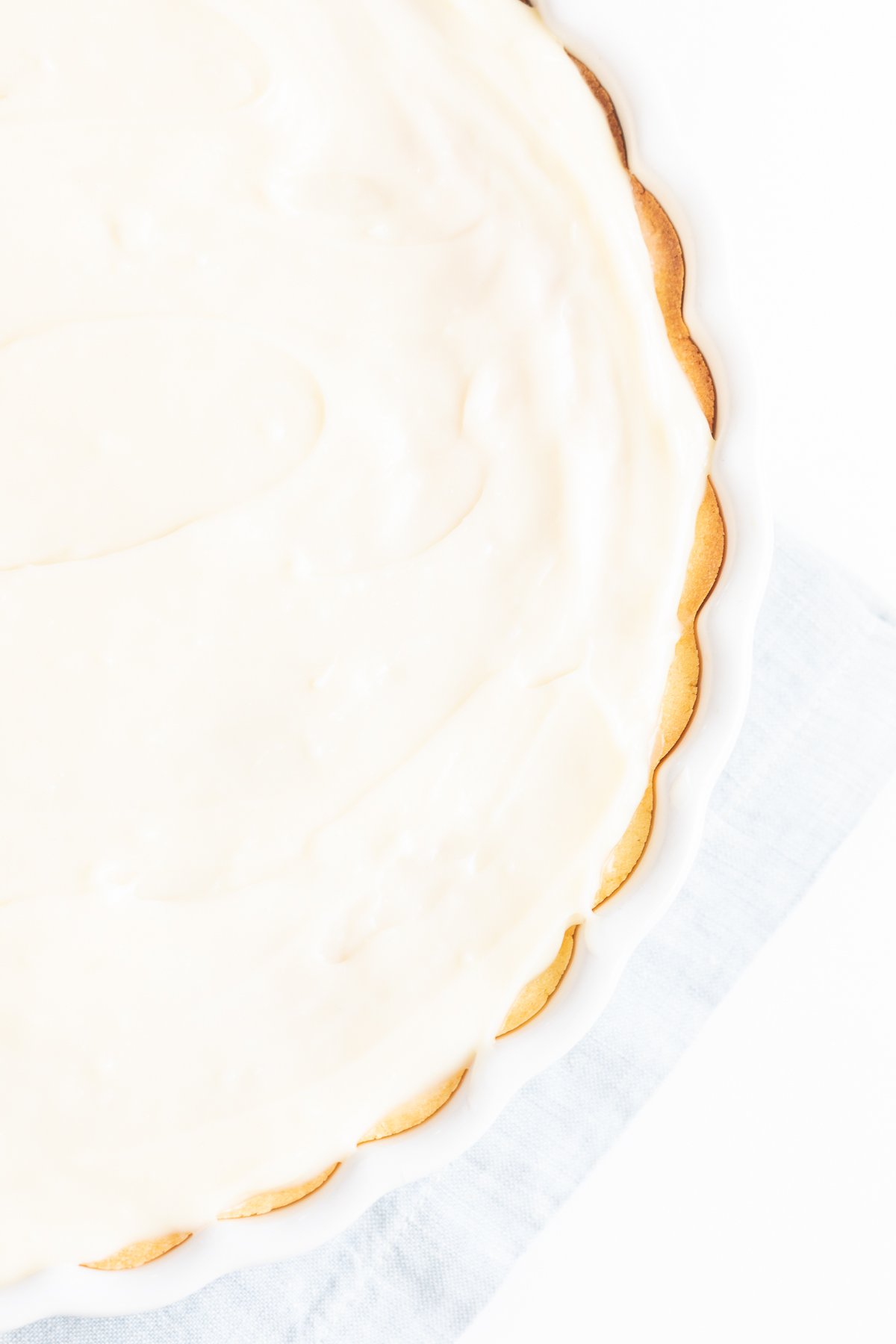 A close-up view of a creamy frosted fruit pizza crust on a white backdrop.