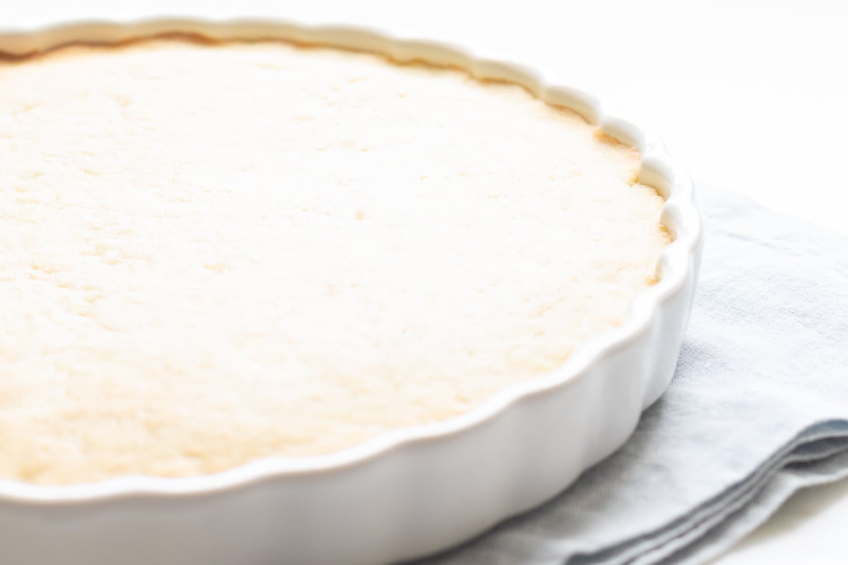 A freshly baked fruit pizza in a white ceramic dish on a linen cloth, complete with an easy fruit pizza glaze.