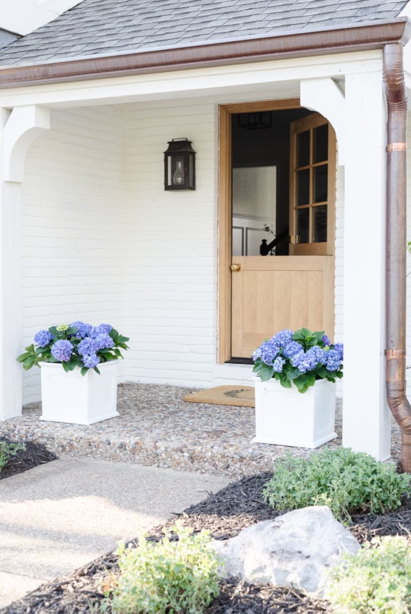 A beautifully decorated white house with breathtaking blue potted flowers on the front porch, offering inspiring decorating tips.