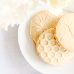 lemon shortbread cookies stamped with flowers, bees and beehives on a white plate