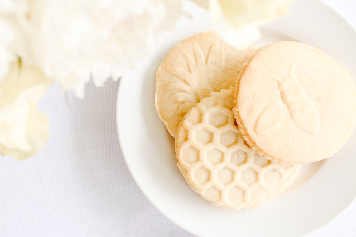 lemon shortbread cookies stamped with flowers, bees and beehives on a white plate