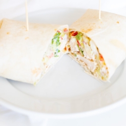 A chicken wrap recipe on a white plate, cut in half.