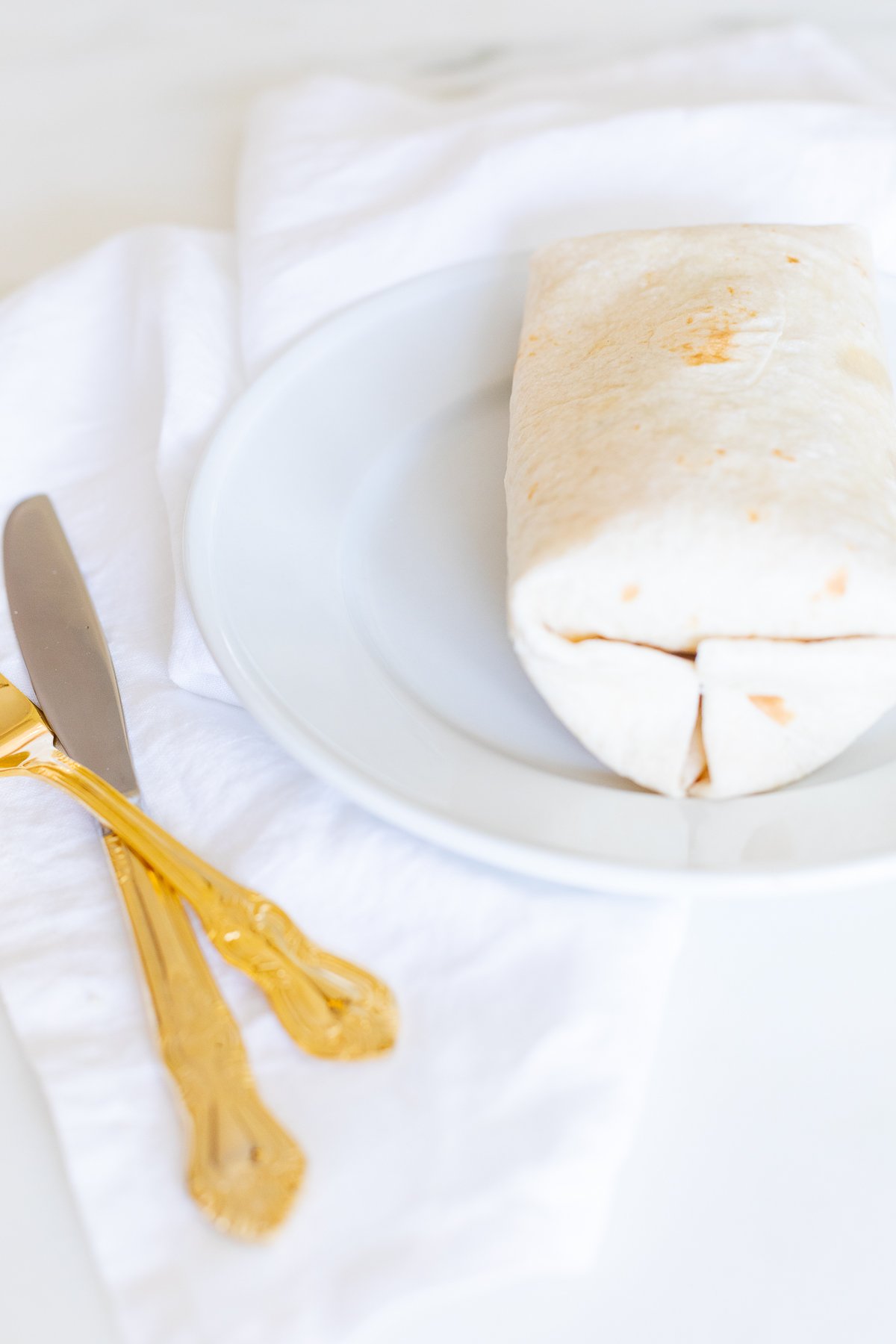 A chicken wrap on a white plate with gold silverware.