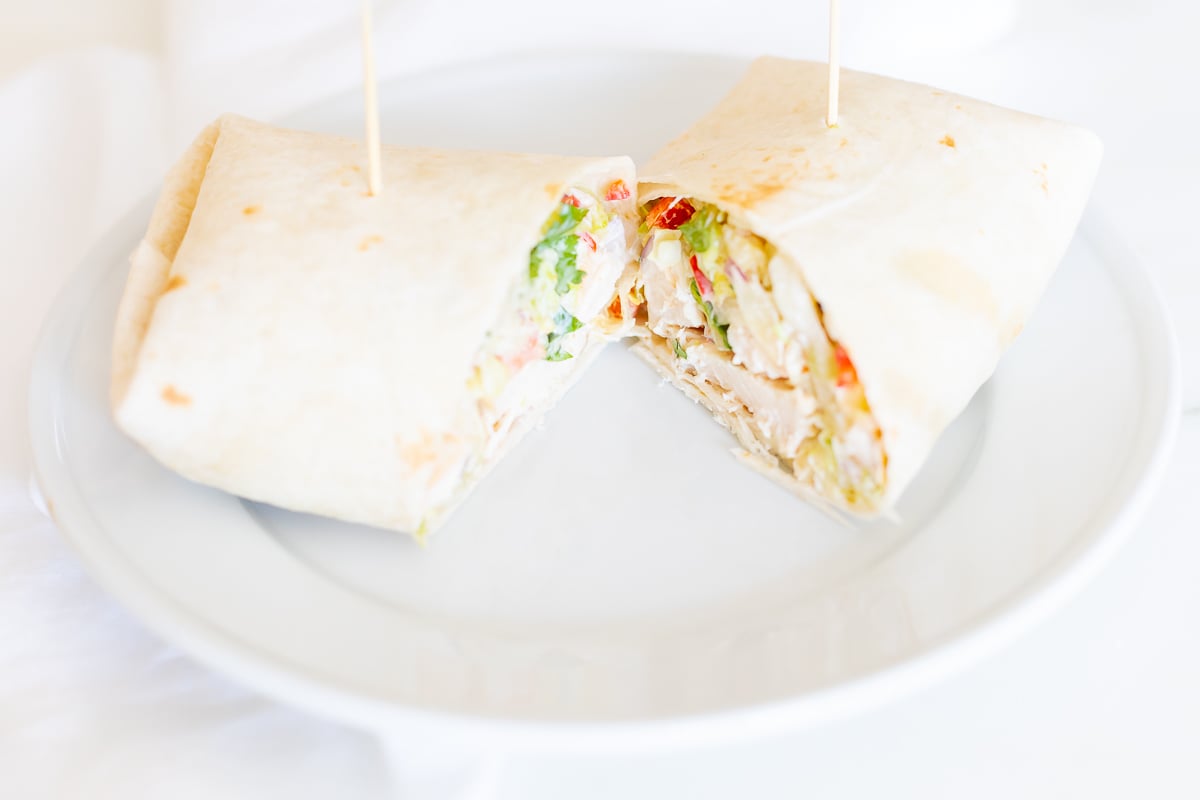 A chicken wrap recipe on a white plate, cut in half.