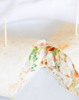 A chicken wrap recipe on a white plate, cut in half.