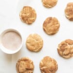 Soft and fluffy snickerdoodle cookies on a white countertop with a bowl of cinnamon and sugar. #easysnickerdoodlecookierecipe #softsnickerdoodlerecipe