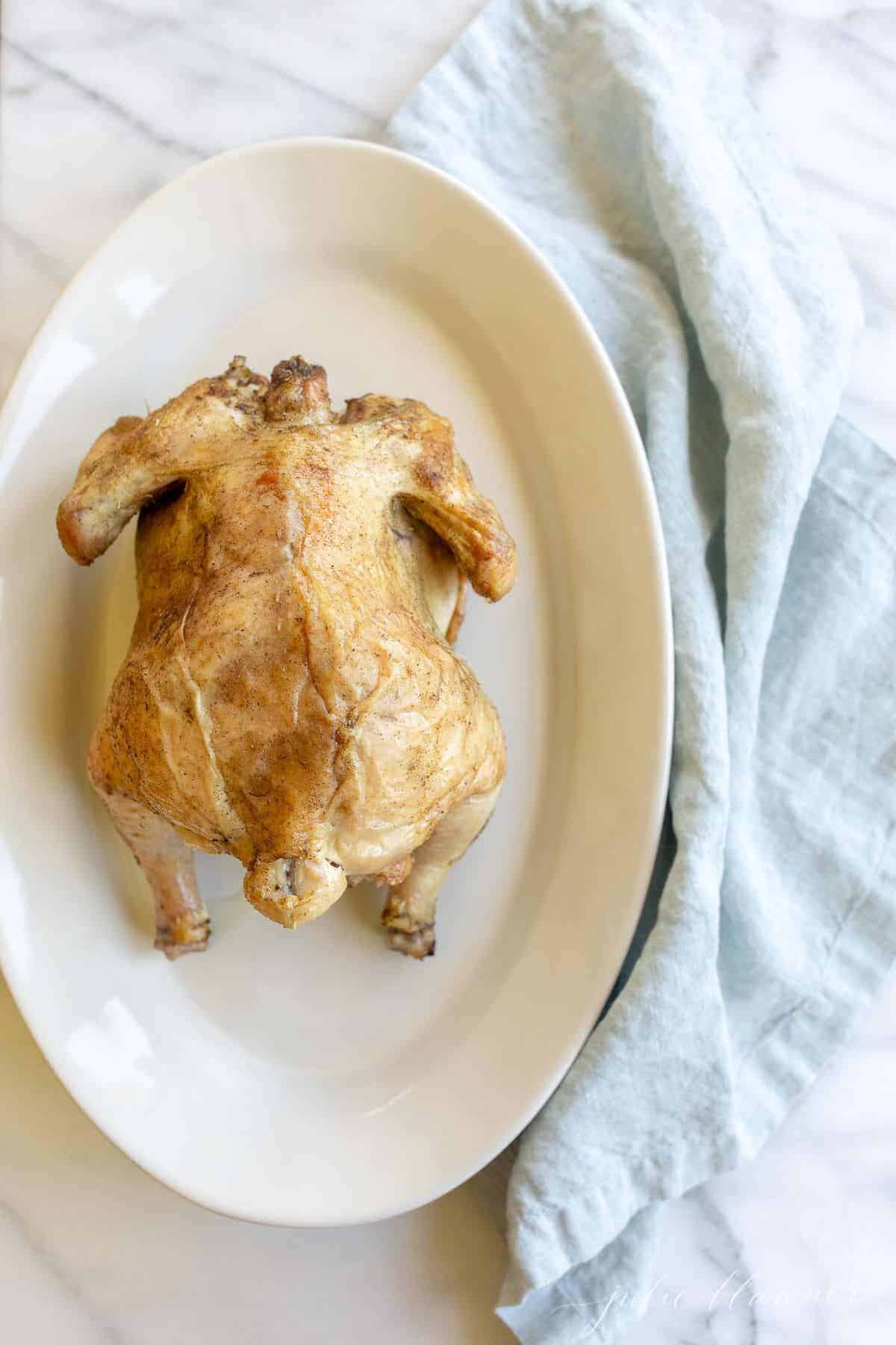 White platter featuring a beer can roasted chicken with golden skin. Blue linen napkin to side. #beercanchicken