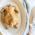 White platter featuring a beer can roasted chicken with golden skin. Blue linen napkin to side. #beercanchicken