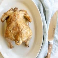 White platter featuring a beer can roasted chicken with golden skin. Blue linen napkin to side. #beercanchicken
