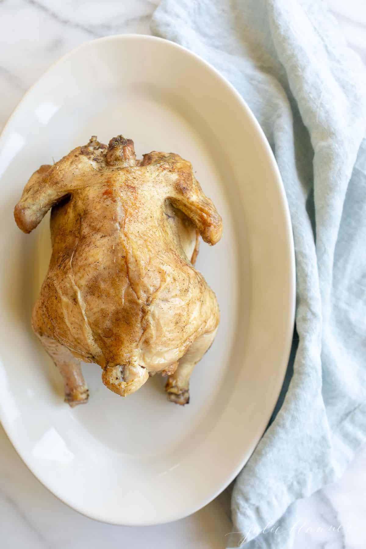 White platter featuring a beer can roasted chicken with golden skin. Blue linen napkin to side. #beercanchicken