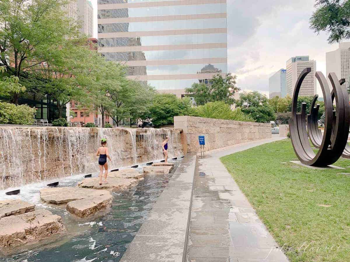 Children running through splash park with high rise in the background in St. Louis