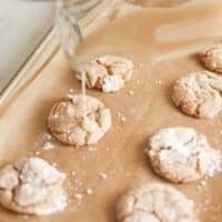 A glass jar pouring apple glaze onto cookies on a gold baking sheet. #appleglaze #appleciderglaze