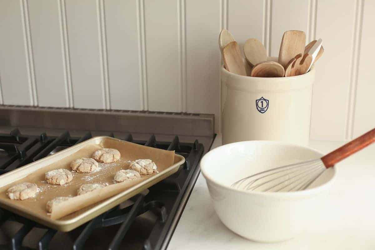 Cookies on a cookie sheet on stovetop, with a bowl of glaze and a whisk. #appleglaze