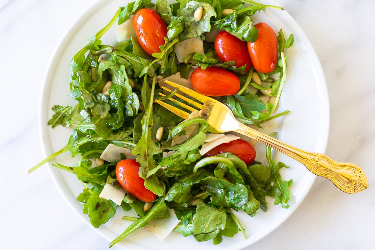 A white plate with insalata mista and a gold fork.