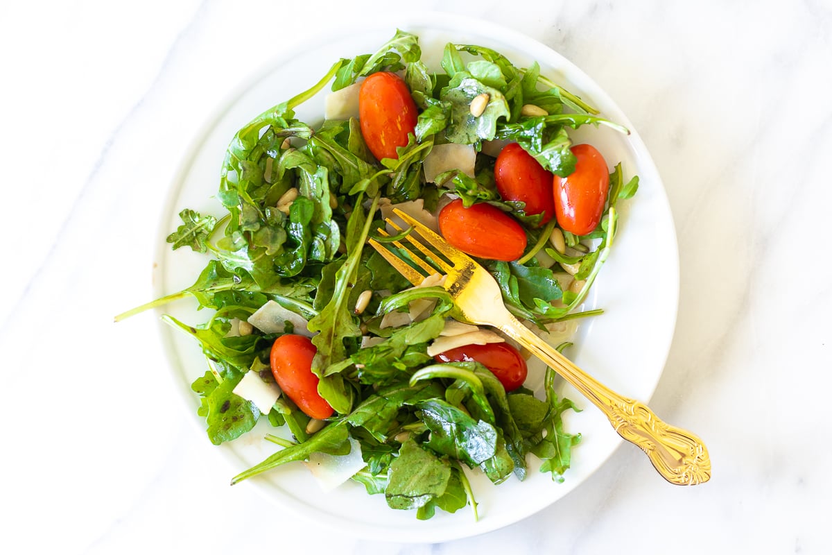 A white plate with insalata mista and a gold fork. 