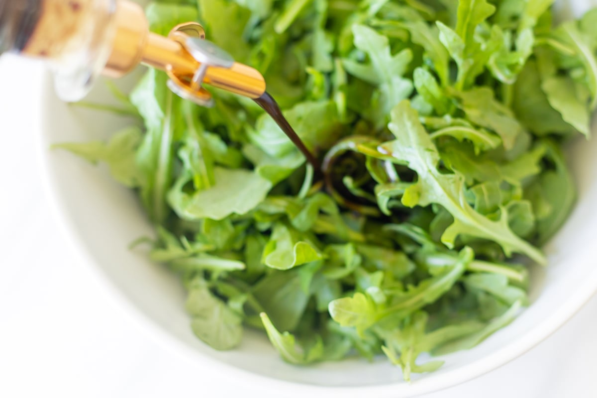 A bowl of arugula with a bottle of homemade vinaigrette being poured over it.