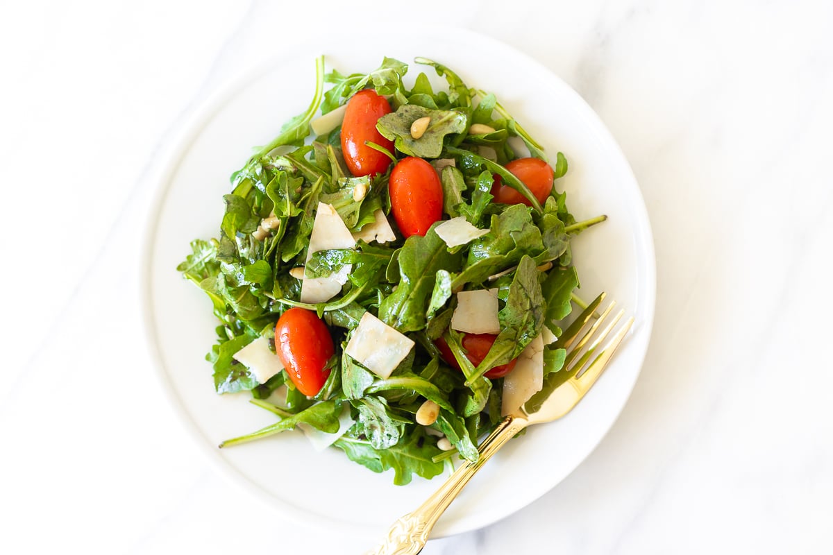 A white plate with insalata mista and a gold fork.