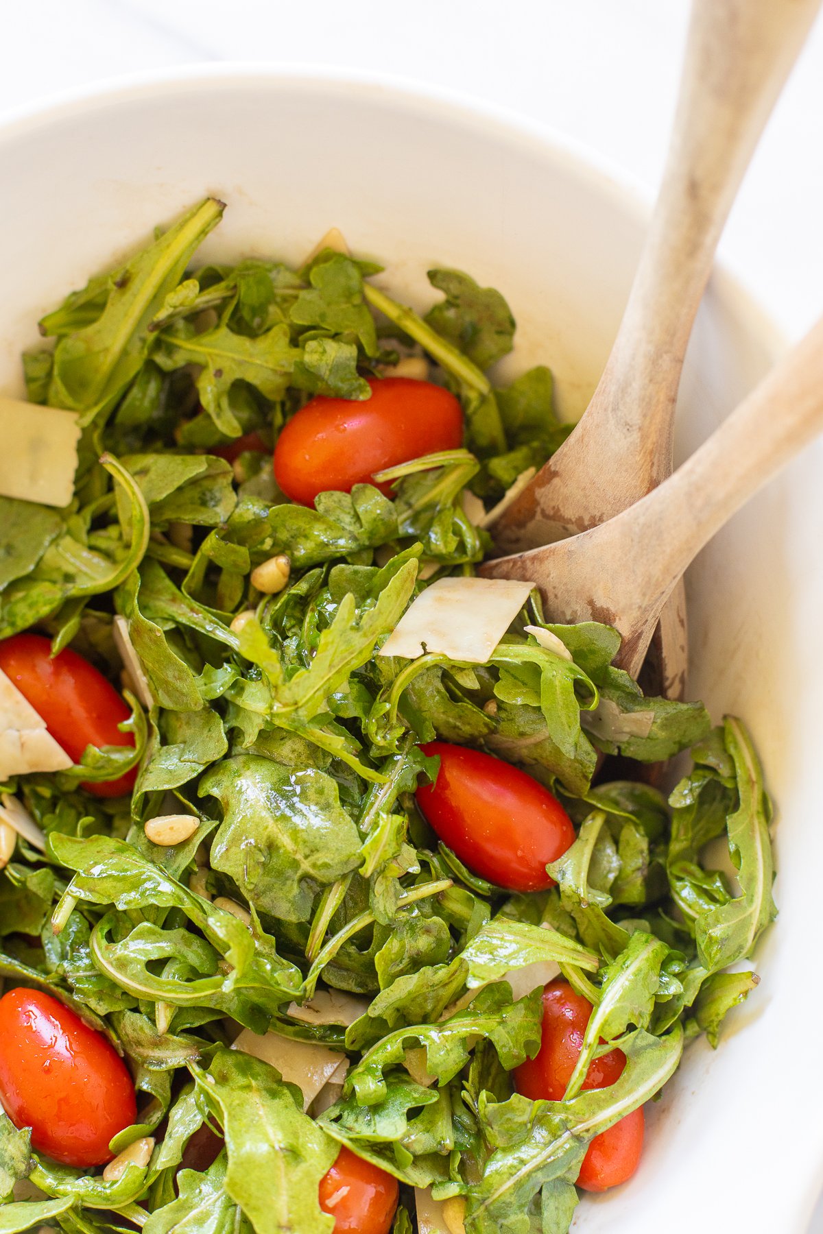 White bowl of insalata mista and wooden spoons on a white countertop