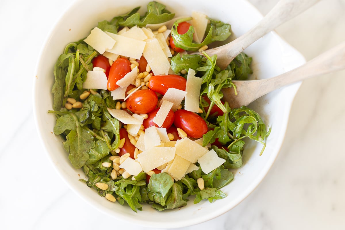 White bowl of insalata mista (mixed salad) and wooden spoons on a white countertop