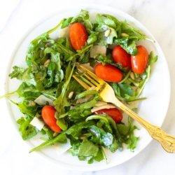 A white plate with insalata mista and a gold fork.