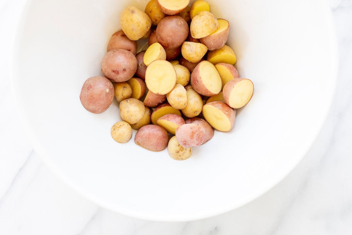 A white bowl filled with whole and halved multicolored baby potatoes on a marble surface, showcasing Italian vegetables.