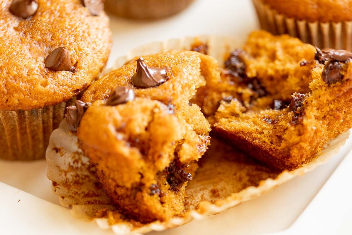 A pumpkin chocolate chip muffin torn in two pieces, resting on the muffin wrapper