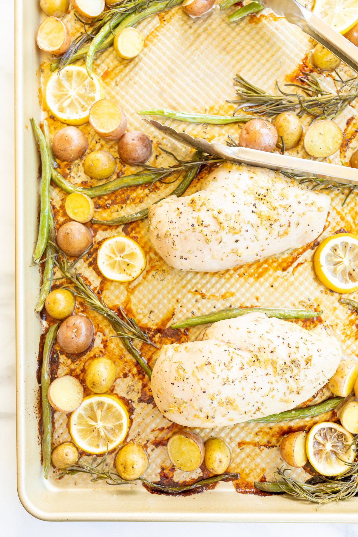 Baked rosemary chicken breasts, lemon slices, and potatoes on a sheet pan.