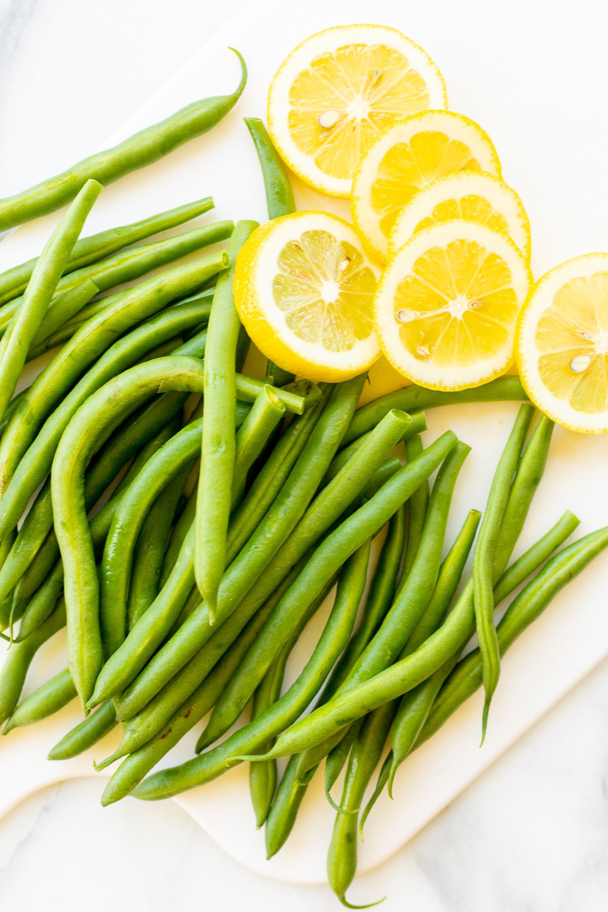 Green beans, rosemary chicken, and sliced lemon rounds arranged on a white cutting board.