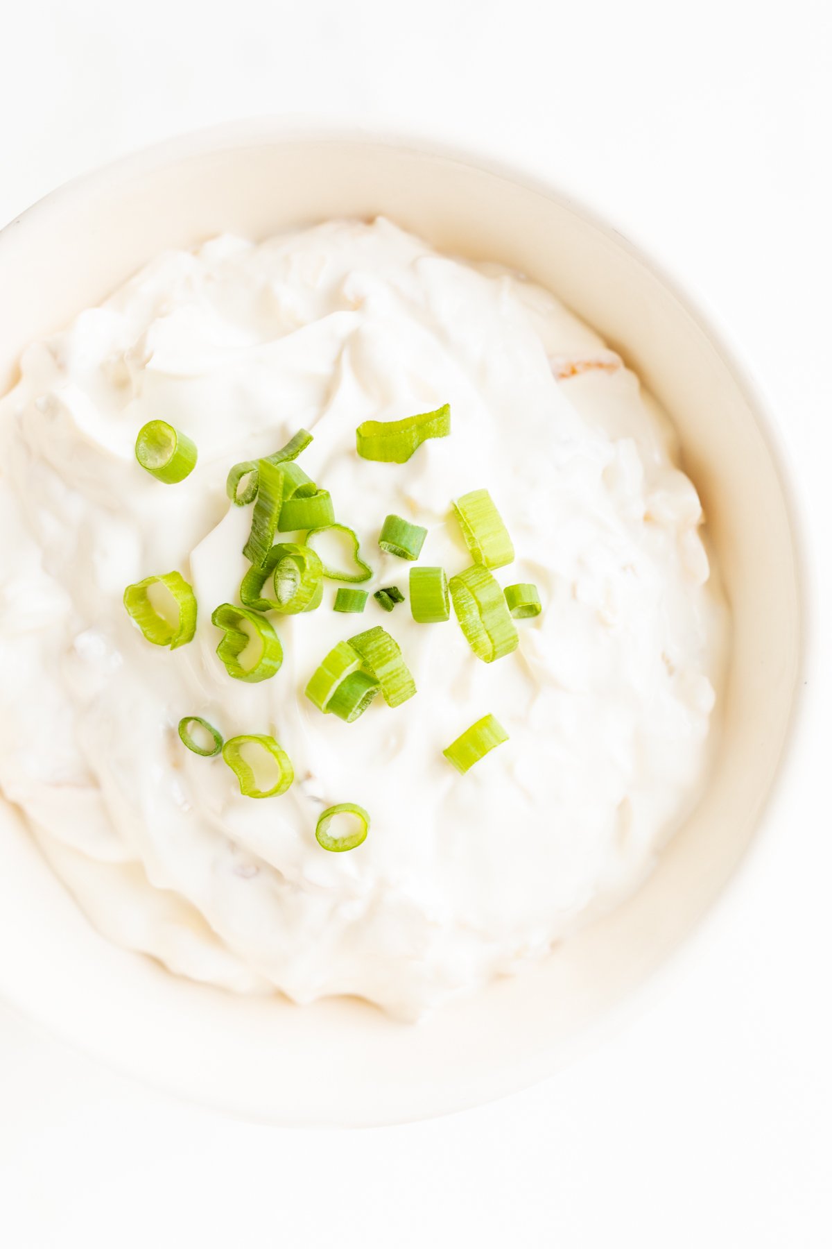 A white bowl full of sour cream dip, topped with chopped green onions.