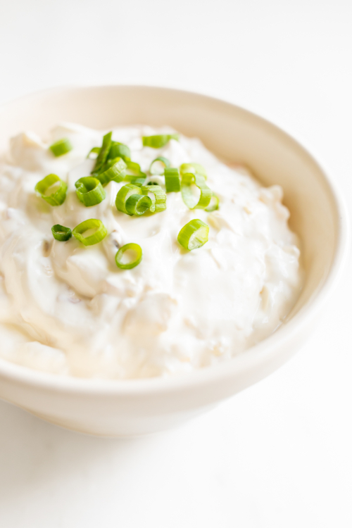 A white bowl full of sour cream dip, topped with chopped green onions.